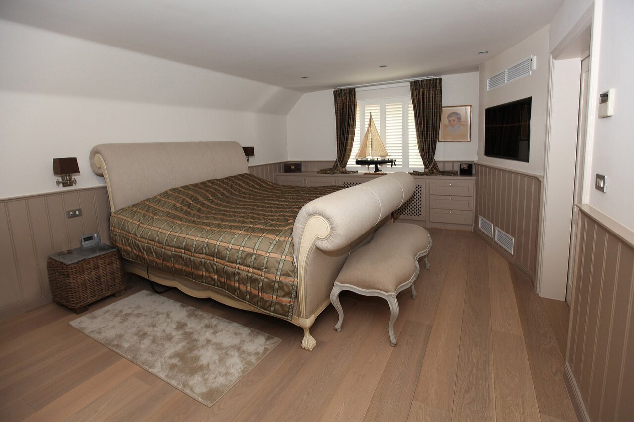 Une chambre avec un lit à tête et pied cintrés, un lambris en bois tout autour et une banquette au pied du lit.