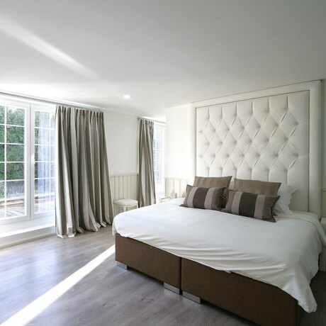 Détail d'une haute tête de lit capitonnée en tissu clair, avec deux coussins rayés devant.