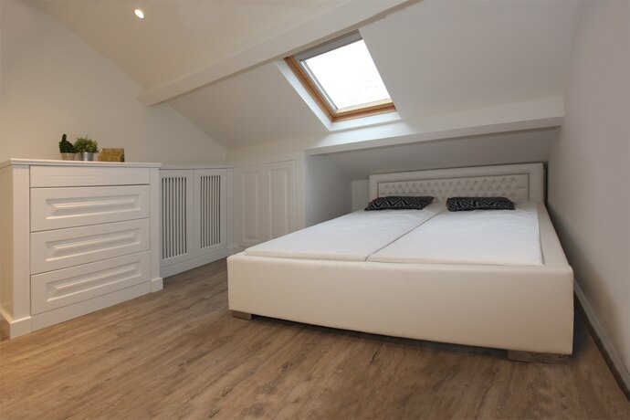 Une chambre claire sous les toits avec une fenêtre de toit, un lit rembourré et des armoires blanches encastrées à lames verticales.