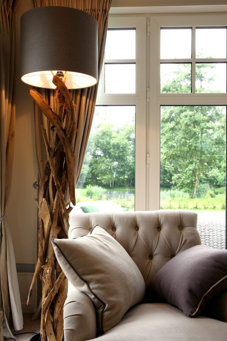 Detail van een gecapitonneerde fauteuil in taupe stof, met een schemerlamp op een voet van drijfhout ernaast.