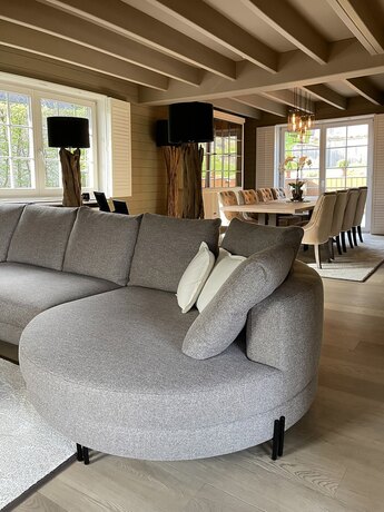 Een ronde grijze hoekzetel met een lage rug, in een kamer met balken en een houten wand.