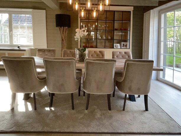 Four velvet chairs at an oak table, seen from behind, with the garden through the window.