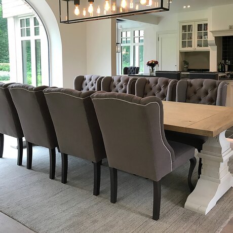A long oak table with buttoned chairs, seen from the head, with the kitchen in the background.