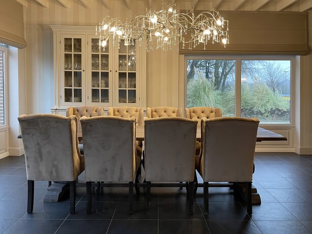 An oak table with velvet chairs in two tones, under a chandelier of branches, in front of glazing onto the garden.