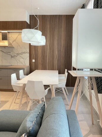 A white dining table with light chairs in a modern space, in front of a wall in walnut and marble.