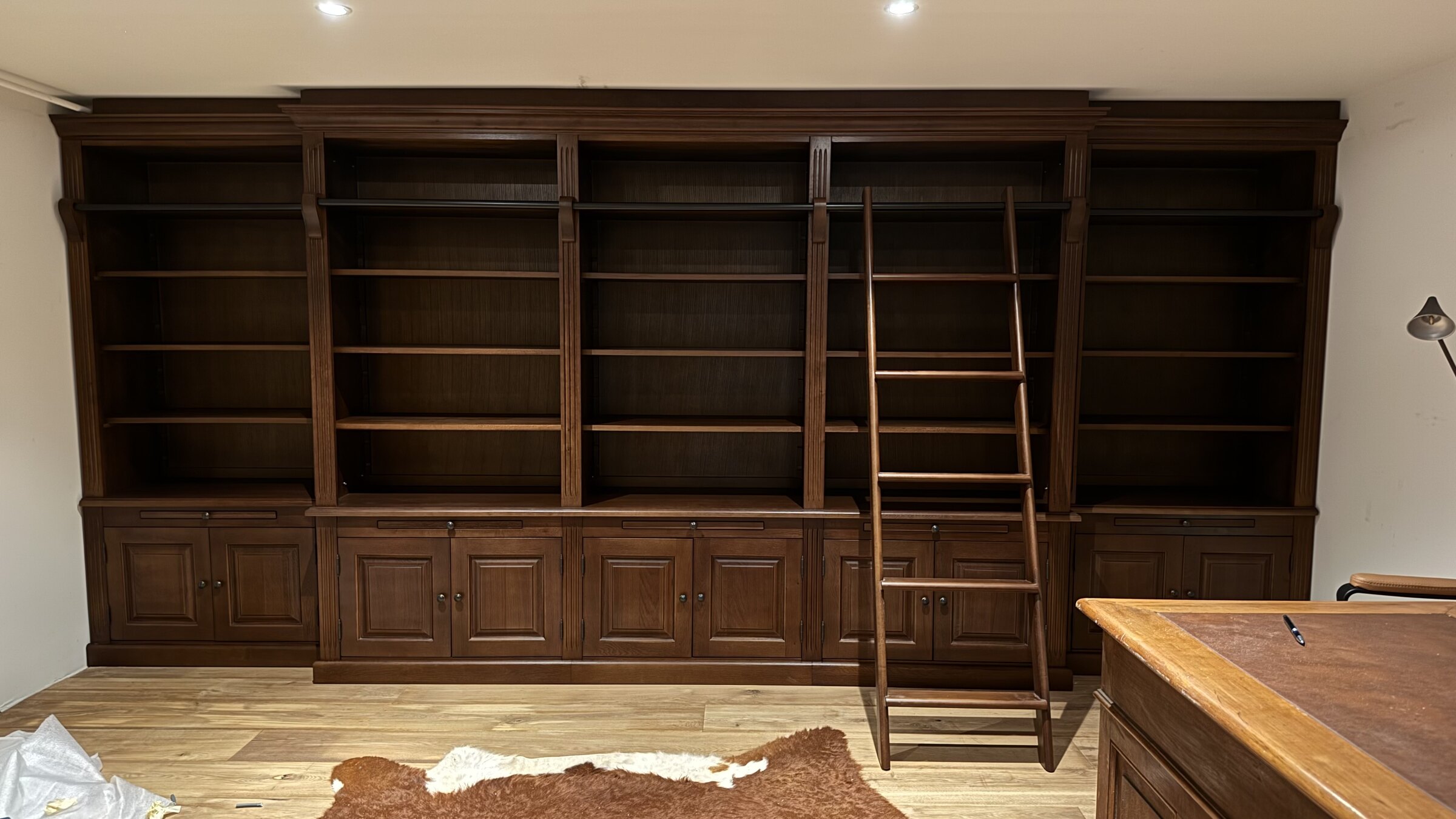 The installed library in dark stained oak, with the sliding ladder in front of it.