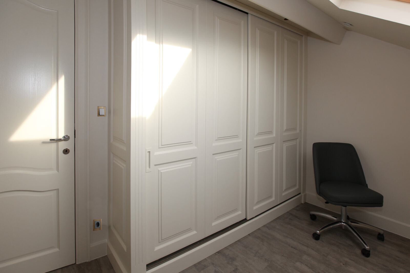 A white cabinet wall with sliding panelled doors, fitted under a sloping ceiling.