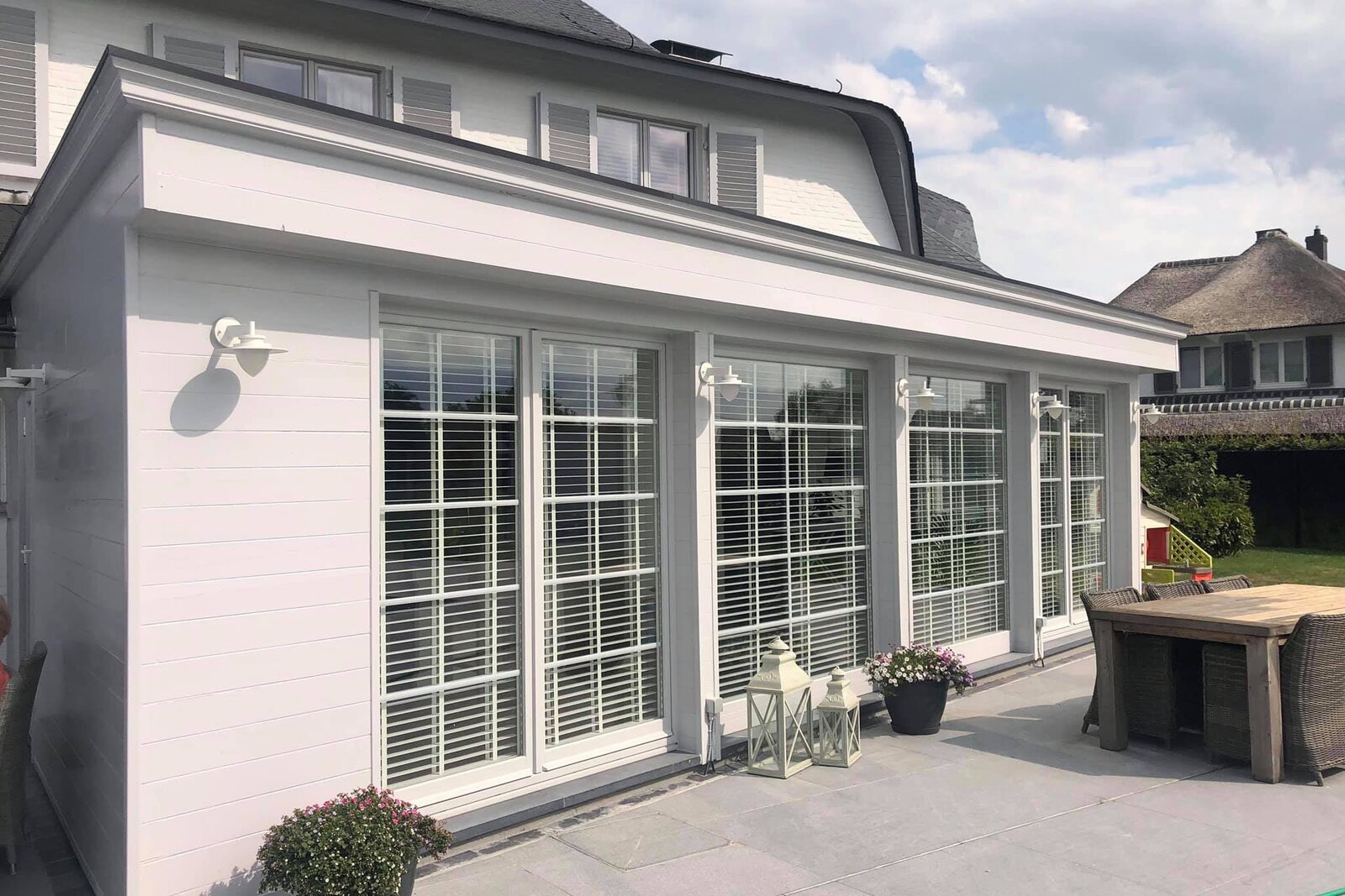 Eine fertige Orangerie mit weißen Fenstern an einer Villa, mit einer Terrasse davor.