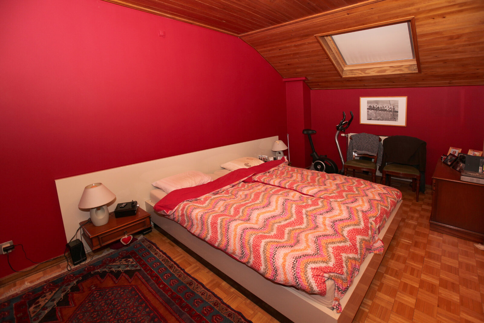 Ein Schlafzimmer mit roter Wand, Holzdecke und einem Teppich.