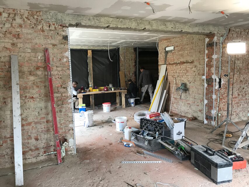 Eine Außenwand bis auf den Rohbau geöffnet, mit Stützen und Material im Raum.