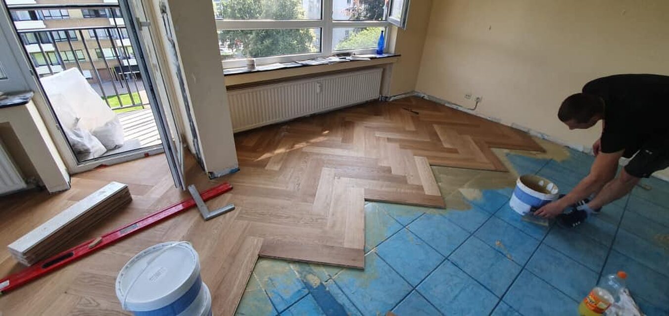Ein Fischgrätparkett, das über den alten Fliesenboden verlegt wird.